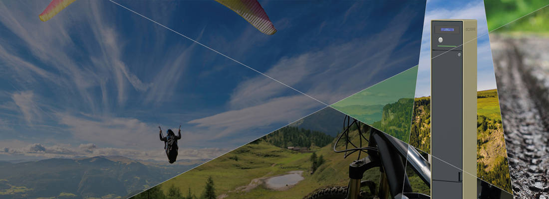 Scame charging station for e-bikes in outdoor environments. Composite image showing a charging station for electric bicycles in an outdoor activity context, with paragliding, mountain biking and mountain trails, highlighting the practicality and sustainability of charging for E-Bike in natural environments.